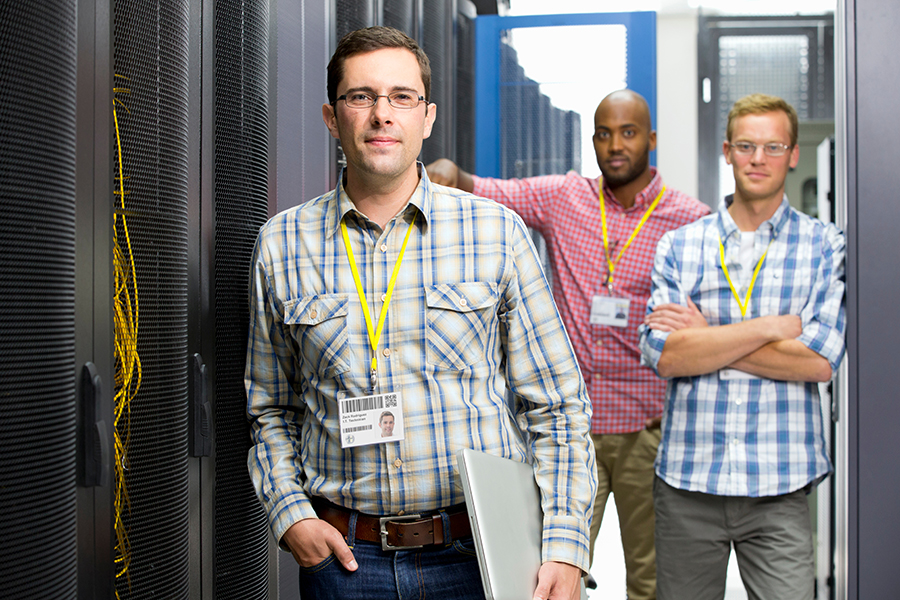 A group of data center managers standing in the middle of a server room looking at the camera